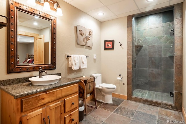 bathroom featuring stone tile floors, toilet, a stall shower, vanity, and baseboards