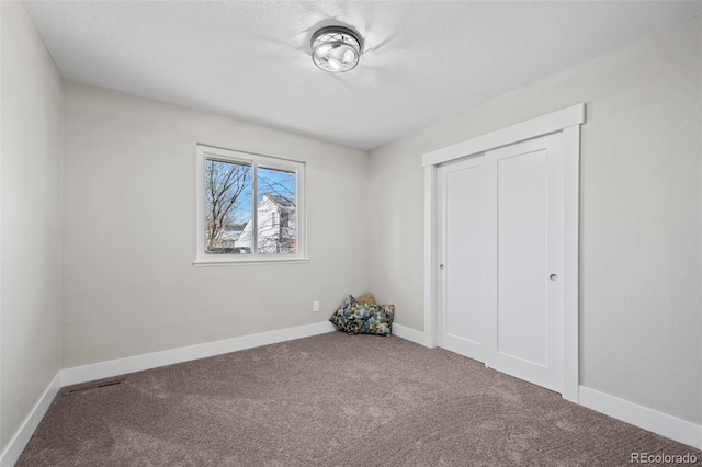 unfurnished bedroom with a textured ceiling, carpet floors, a closet, and baseboards