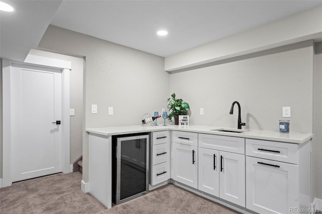 kitchen featuring beverage cooler, white cabinetry, light countertops, and a sink