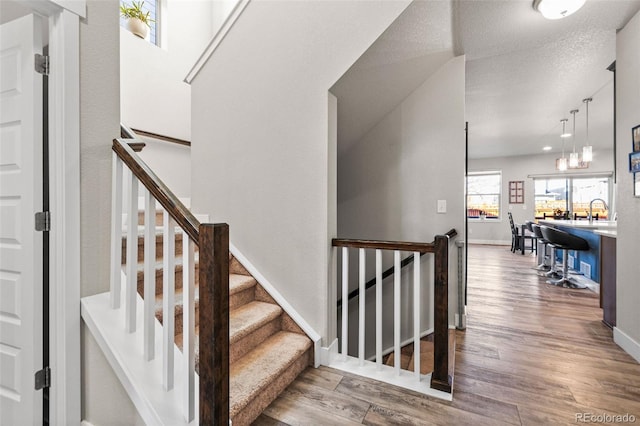 staircase with a textured ceiling, baseboards, and wood finished floors