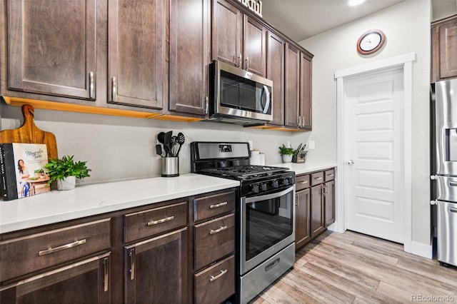 kitchen with stainless steel appliances, dark brown cabinets, light countertops, and light wood finished floors