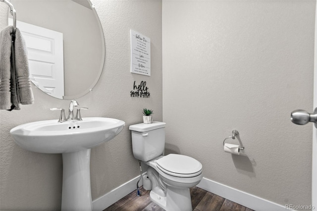 half bath with toilet, wood finished floors, and baseboards