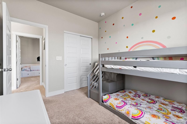 bedroom with a closet, light carpet, and baseboards