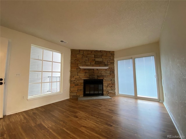 unfurnished living room with hardwood / wood-style floors, a stone fireplace, and a textured ceiling