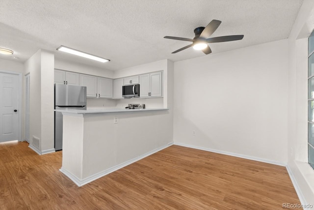 kitchen with light hardwood / wood-style flooring, a textured ceiling, appliances with stainless steel finishes, kitchen peninsula, and ceiling fan