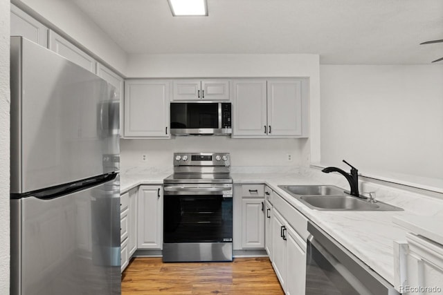 kitchen with stainless steel appliances, light stone countertops, sink, and light wood-type flooring