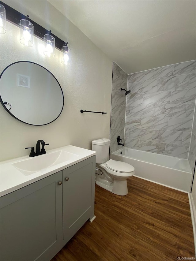 full bathroom featuring hardwood / wood-style flooring, vanity, tiled shower / bath combo, and toilet