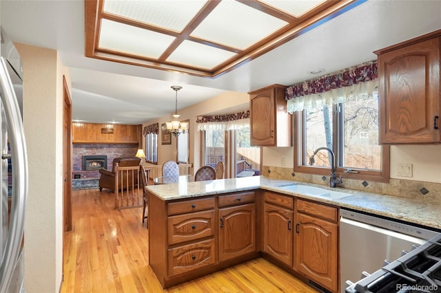 kitchen featuring sink, a brick fireplace, kitchen peninsula, pendant lighting, and appliances with stainless steel finishes