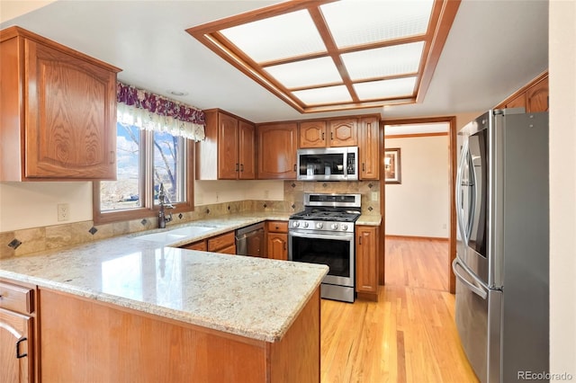 kitchen featuring sink, light stone countertops, light hardwood / wood-style floors, kitchen peninsula, and stainless steel appliances