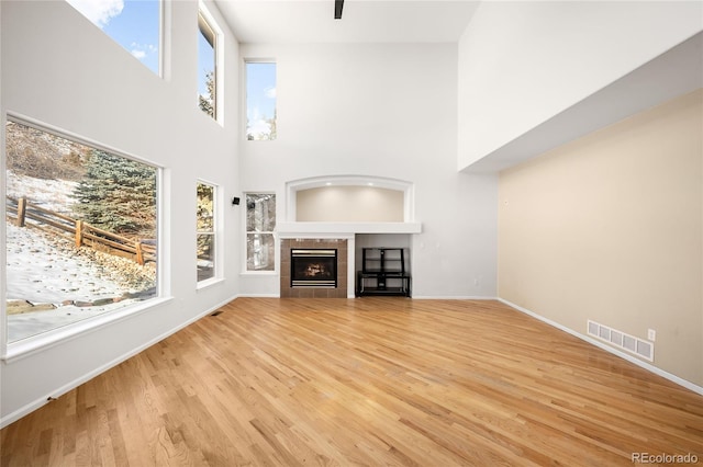 unfurnished living room with a high ceiling, a tile fireplace, and light hardwood / wood-style flooring