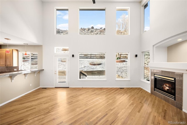 unfurnished living room featuring light wood-type flooring, a towering ceiling, and a tile fireplace