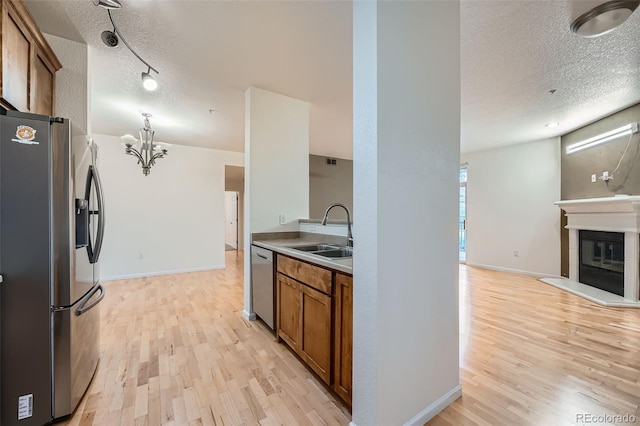 kitchen with sink, a chandelier, light hardwood / wood-style floors, a textured ceiling, and appliances with stainless steel finishes