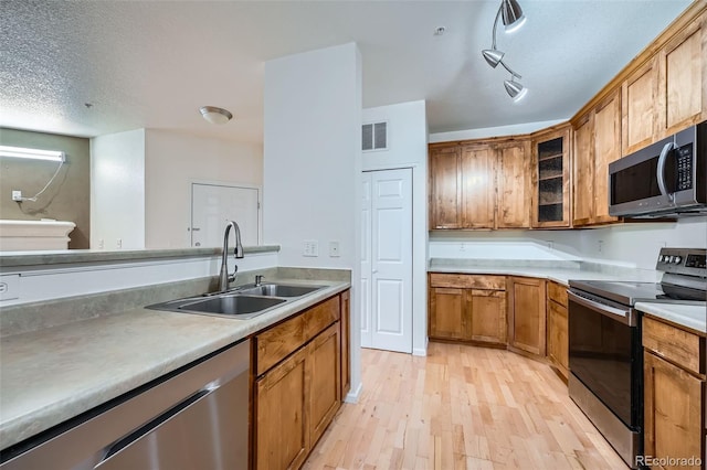 kitchen featuring appliances with stainless steel finishes, track lighting, a textured ceiling, sink, and light hardwood / wood-style floors