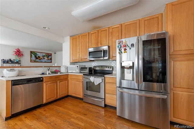 2246 S Ensenada St, Aurora, CO 80013 - kitchen featuring appliances with stainless steel finishes, a sink, light wood-style floors, decorative backsplash, and a peninsula