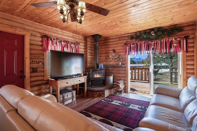 living room featuring wood finished floors, rustic walls, wood ceiling, ceiling fan, and a wood stove