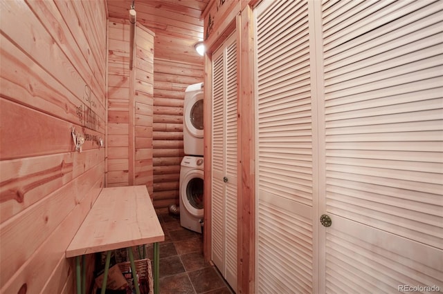 laundry area featuring log walls, stone finish floor, stacked washer / drying machine, wooden ceiling, and laundry area