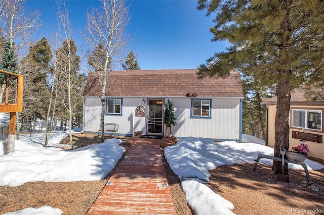 snow covered property with an outdoor structure and roof with shingles