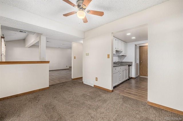 unfurnished living room featuring a textured ceiling, dark colored carpet, ceiling fan, and sink