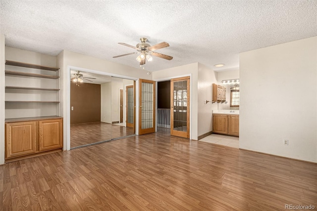 unfurnished living room featuring a textured ceiling, ceiling fan, light hardwood / wood-style floors, and french doors