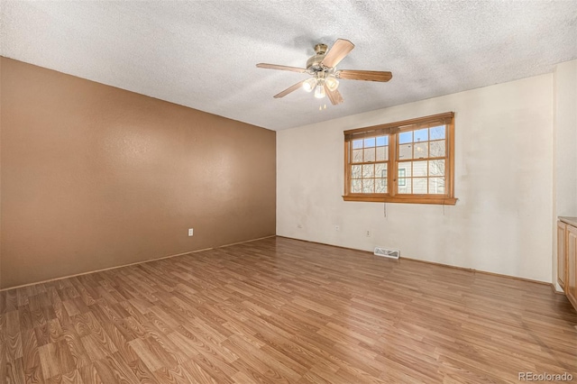 unfurnished room with a textured ceiling, light wood-type flooring, and ceiling fan