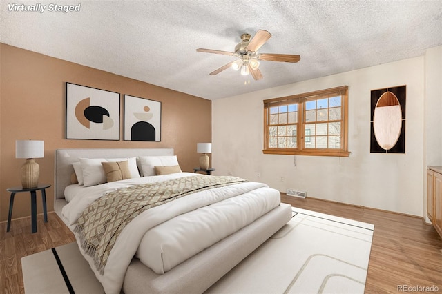 bedroom with a textured ceiling, ceiling fan, and light hardwood / wood-style flooring