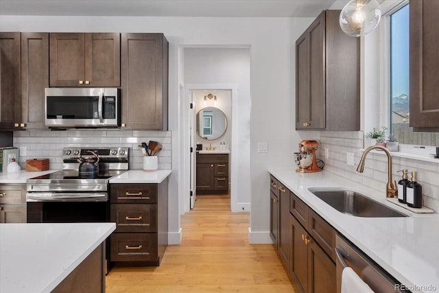 kitchen featuring sink, hanging light fixtures, stainless steel appliances, tasteful backsplash, and light hardwood / wood-style floors