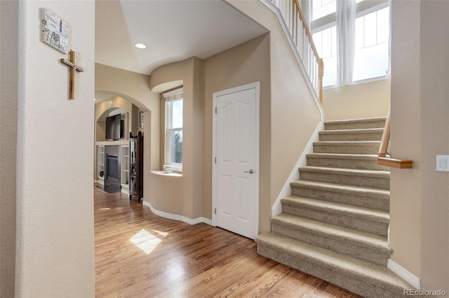 staircase featuring baseboards, arched walkways, a glass covered fireplace, and wood finished floors