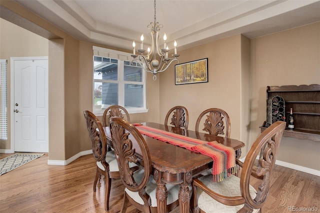 dining space with baseboards, light wood-style flooring, a tray ceiling, and a chandelier