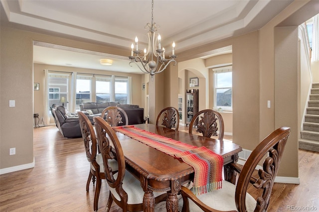 dining room with arched walkways, a tray ceiling, a chandelier, and light wood-style floors
