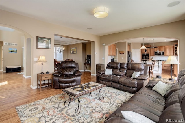 living area featuring arched walkways, baseboards, light wood-type flooring, and visible vents