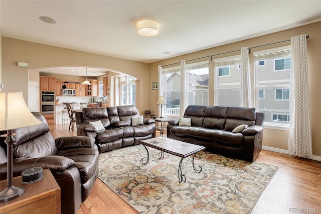 living area featuring baseboards, arched walkways, light wood finished floors, and a healthy amount of sunlight
