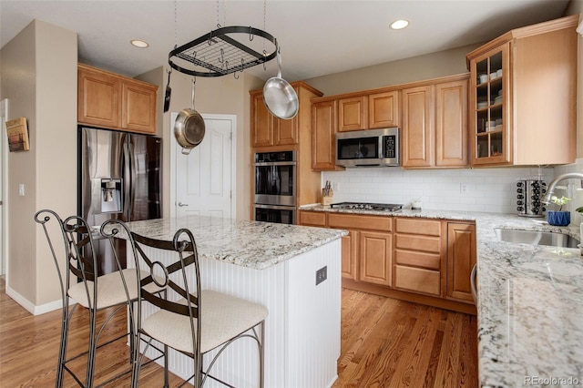 kitchen featuring a kitchen island, light stone countertops, a sink, light wood-style flooring, and appliances with stainless steel finishes