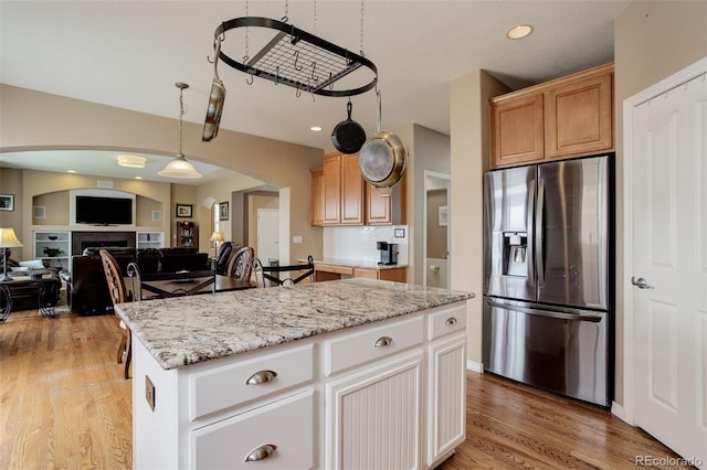 kitchen with light stone counters, stainless steel fridge, light wood-style floors, arched walkways, and open floor plan