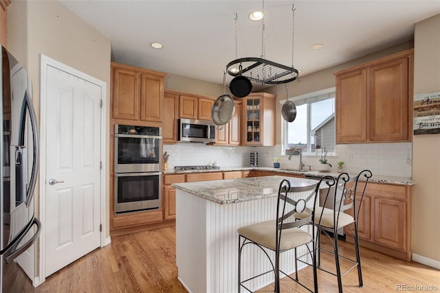 kitchen with a sink, light wood-style flooring, appliances with stainless steel finishes, and a kitchen island