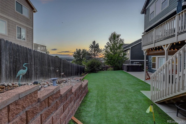 yard at dusk with a patio, a fenced backyard, stairway, and a deck