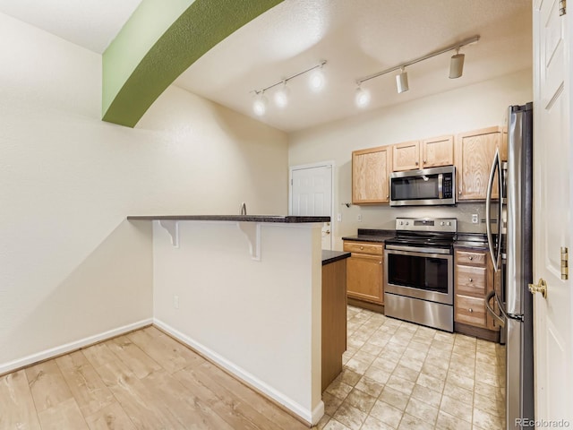 9896 W Freiburg Dr Unit 1D, Littleton, CO 80127 - kitchen featuring appliances with stainless steel finishes, a peninsula, a kitchen breakfast bar, light brown cabinets, and rail lighting