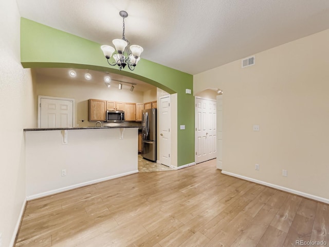 9896 W Freiburg Dr Unit 1D, Littleton, CO 80127 - kitchen featuring appliances with stainless steel finishes, a chandelier, dark countertops, a breakfast bar area, and a peninsula