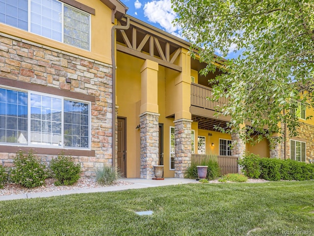 9896 W Freiburg Dr Unit 1D, Littleton, CO 80127 - view of exterior entry featuring a balcony, stucco siding, stone siding, and a lawn