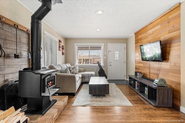 living room featuring wood-type flooring, a wood stove, a textured ceiling, and wooden walls