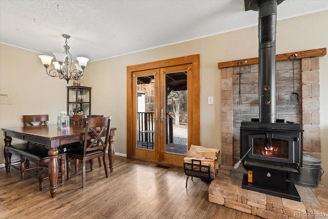 dining area with french doors, a chandelier, a textured ceiling, a wood stove, and hardwood / wood-style flooring