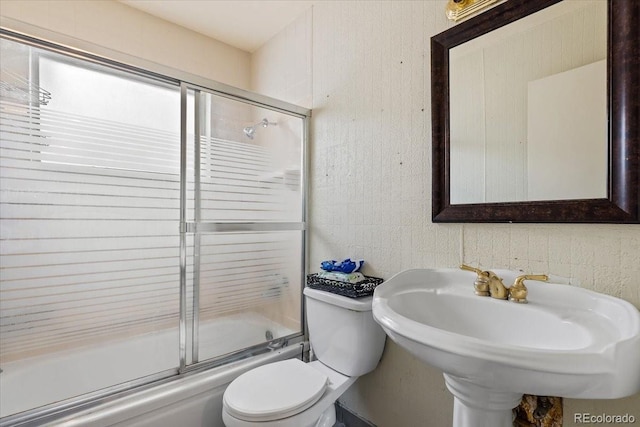 full bathroom featuring toilet, bath / shower combo with glass door, and sink