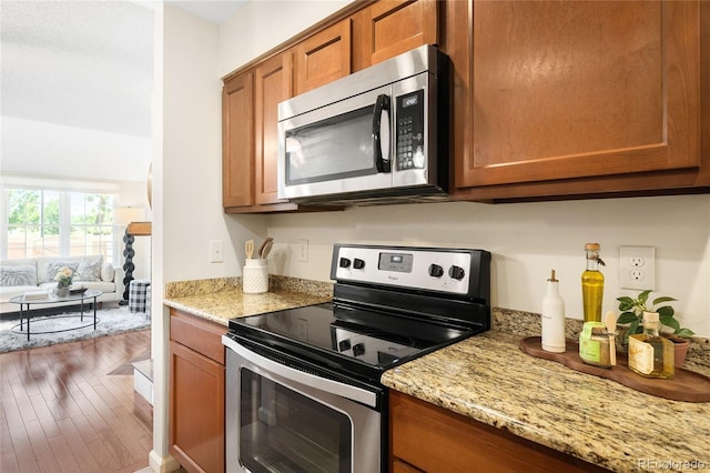 7373 E Iowa Ave Unit 1124, Denver, CO 80231 - kitchen featuring stainless steel appliances, brown cabinetry, light stone counters, and wood finished floors