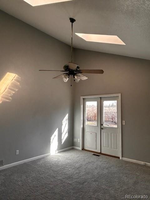 empty room featuring visible vents, baseboards, lofted ceiling with skylight, carpet flooring, and a ceiling fan