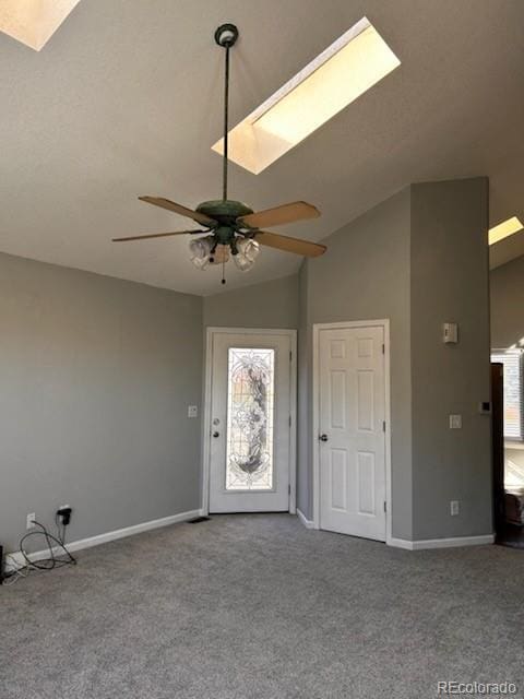 interior space with baseboards, carpet floors, ceiling fan, and vaulted ceiling with skylight