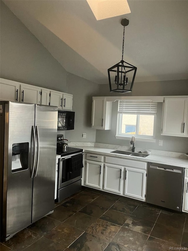 kitchen featuring light countertops, vaulted ceiling with skylight, white cabinets, stainless steel appliances, and a sink