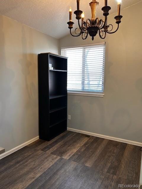 empty room with a textured ceiling, an inviting chandelier, baseboards, dark wood-style flooring, and vaulted ceiling