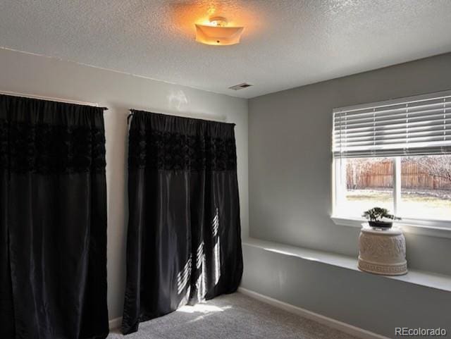 carpeted spare room with visible vents, a textured ceiling, and baseboards