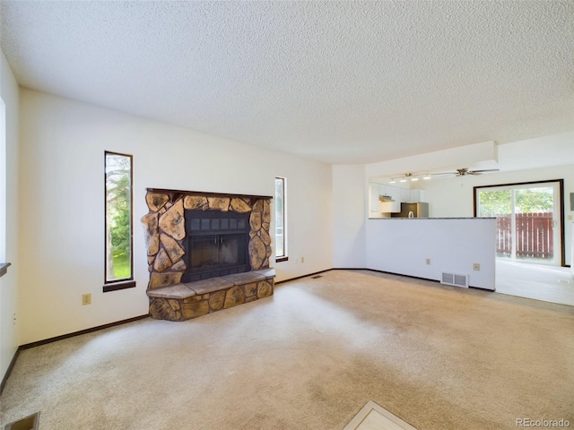 unfurnished living room featuring carpet flooring, ceiling fan, a textured ceiling, and a stone fireplace