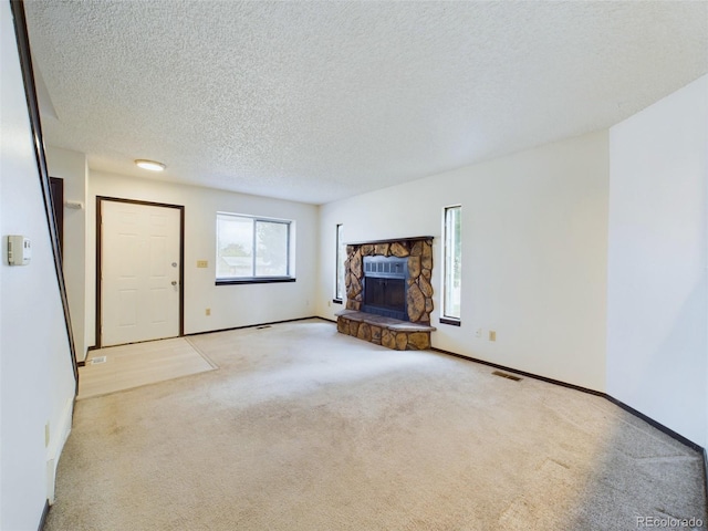 unfurnished living room featuring light carpet, a textured ceiling, and a stone fireplace