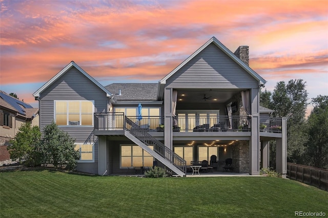 back house at dusk featuring a lawn, ceiling fan, a patio area, and a deck